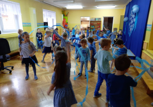 Dzieci improwizują do utworu muzycznego tańcząc z paskami niebieskiej bibuły